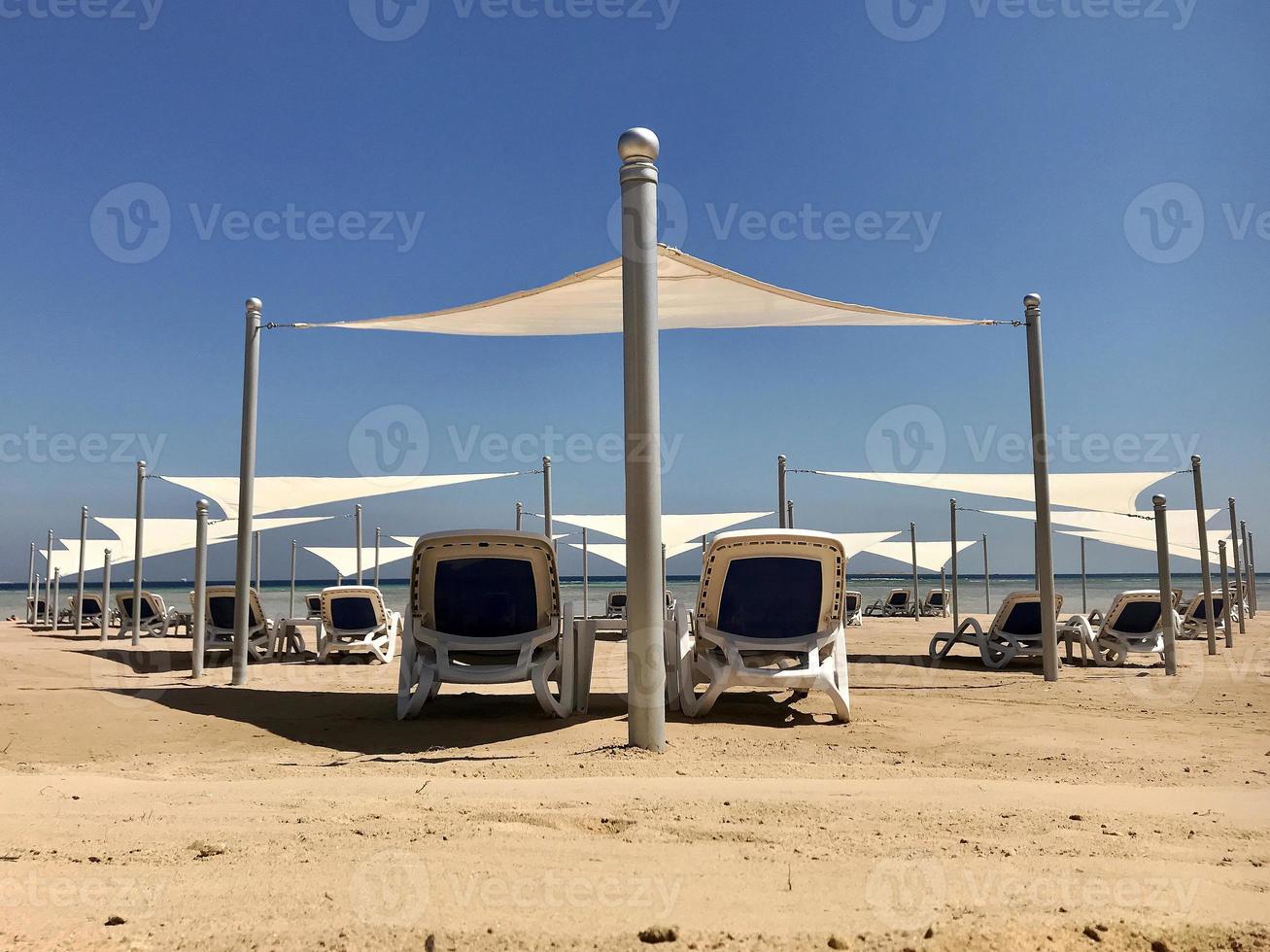 chaise longue élégante dans le sable jaune au soleil transat sur la plage en été sous le ciel ouvert photo
