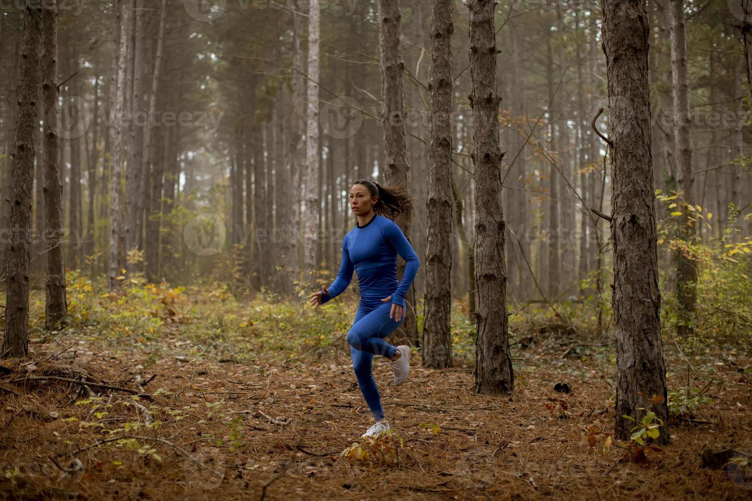 Jeune femme courant sur le sentier forestier à l'automne photo