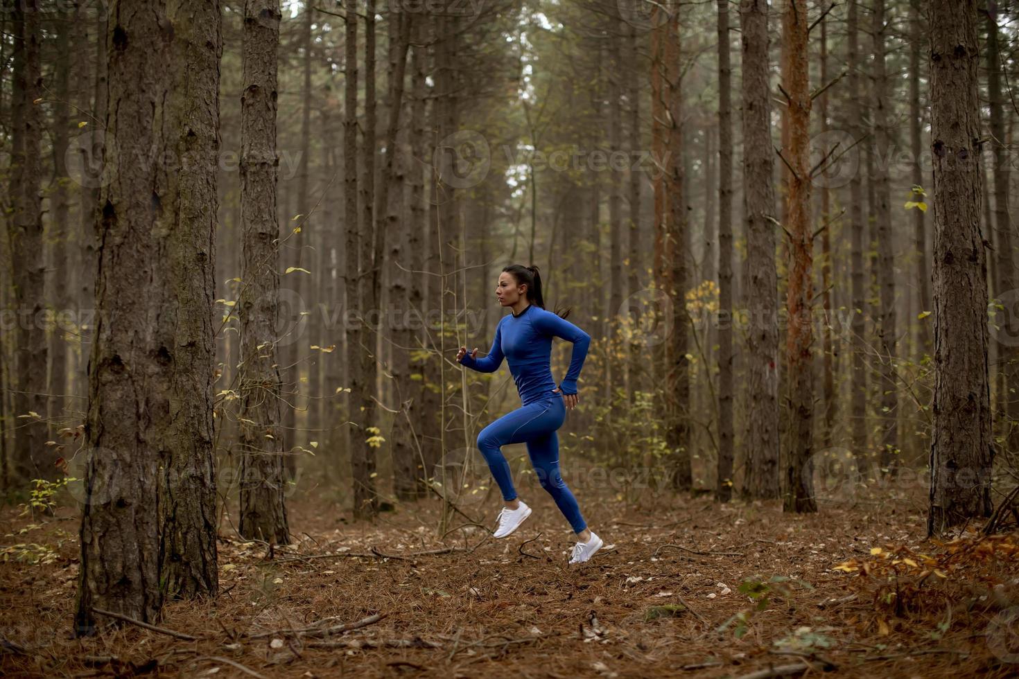 Jeune femme courant sur le sentier forestier à l'automne photo