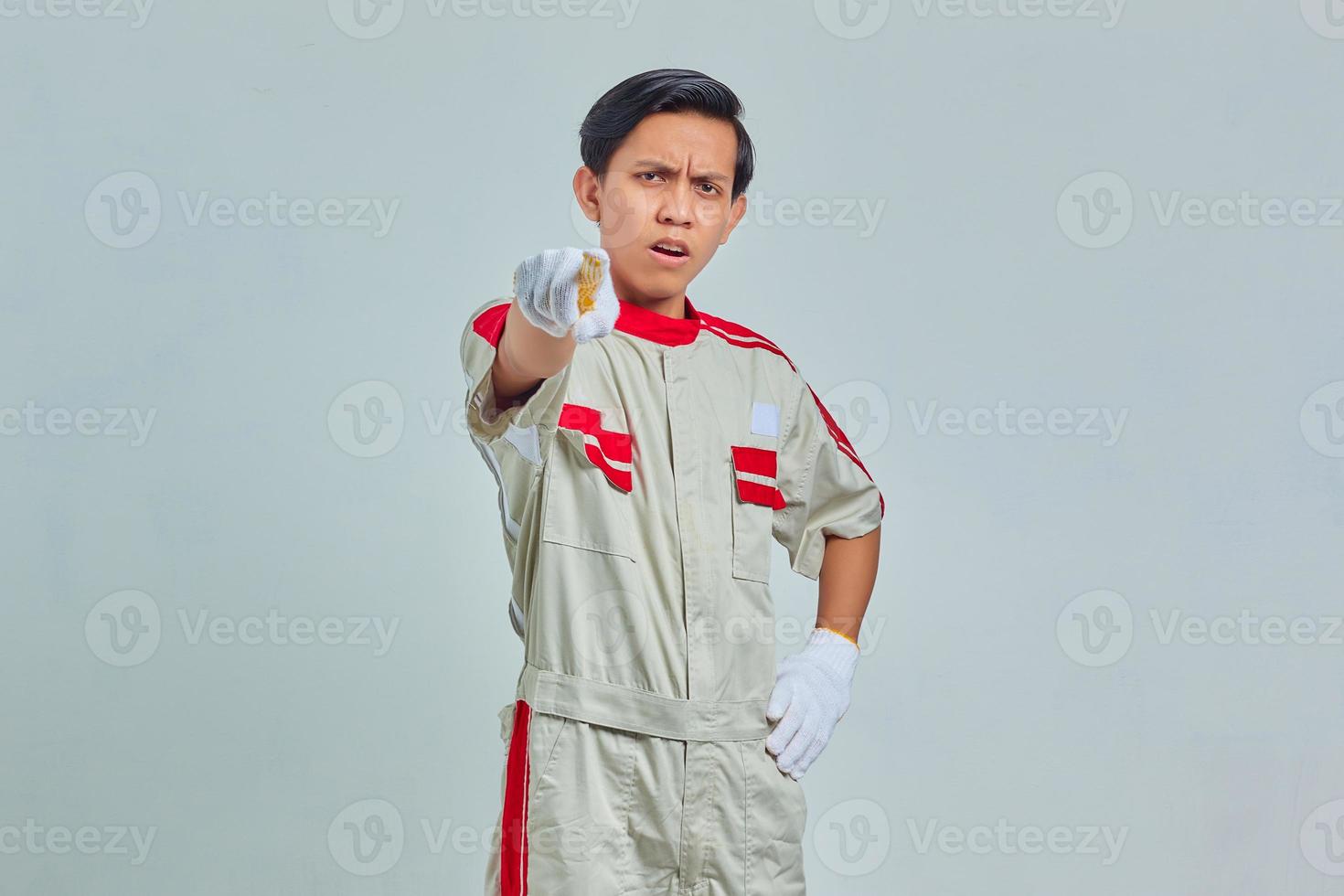 Portrait d'un bel homme surpris portant un uniforme mécanique pointant le doigt et la bouche ouverts sur fond gris photo