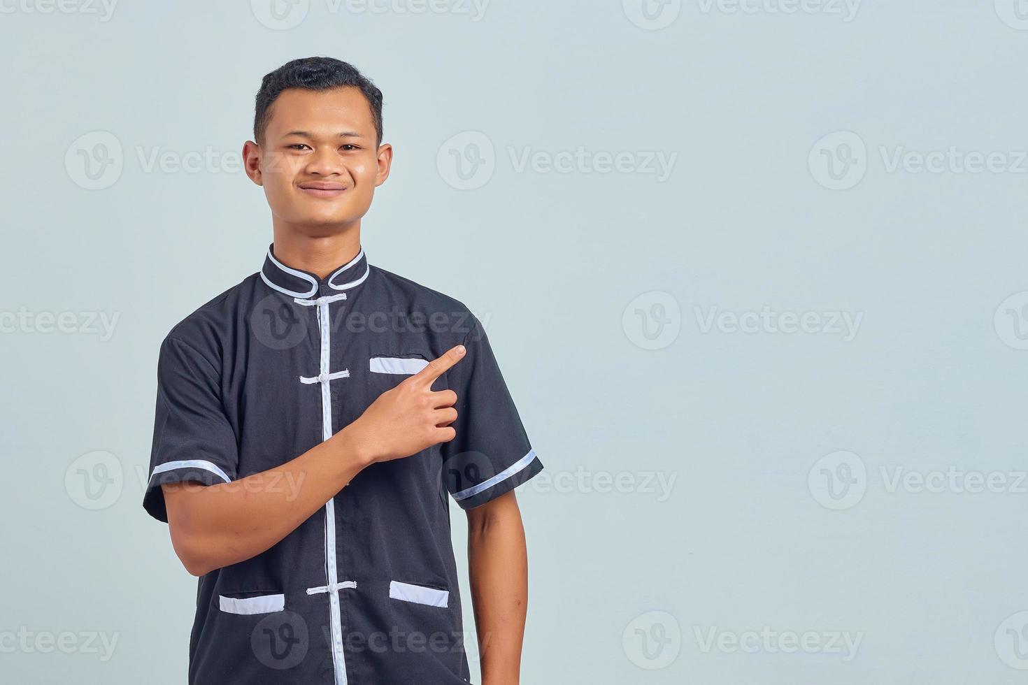 Portrait d'un jeune homme asiatique souriant portant un uniforme de karaté et pointant sur le côté sur fond gris photo