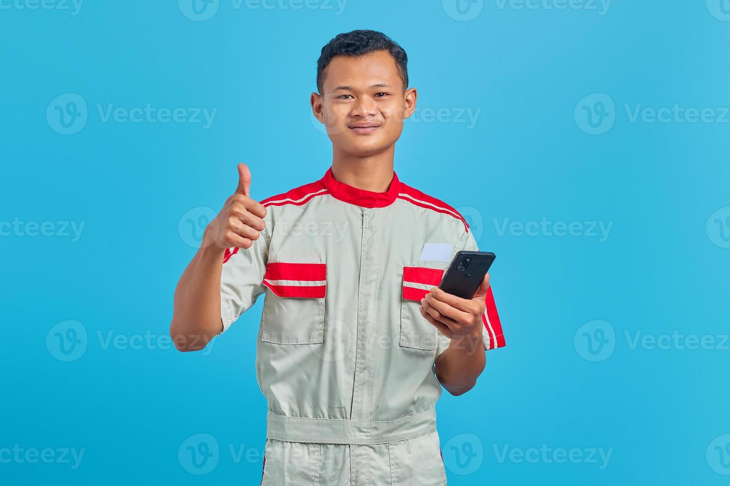 Portrait de jeune mécanicien souriant montrant le geste du pouce isolé sur fond bleu photo