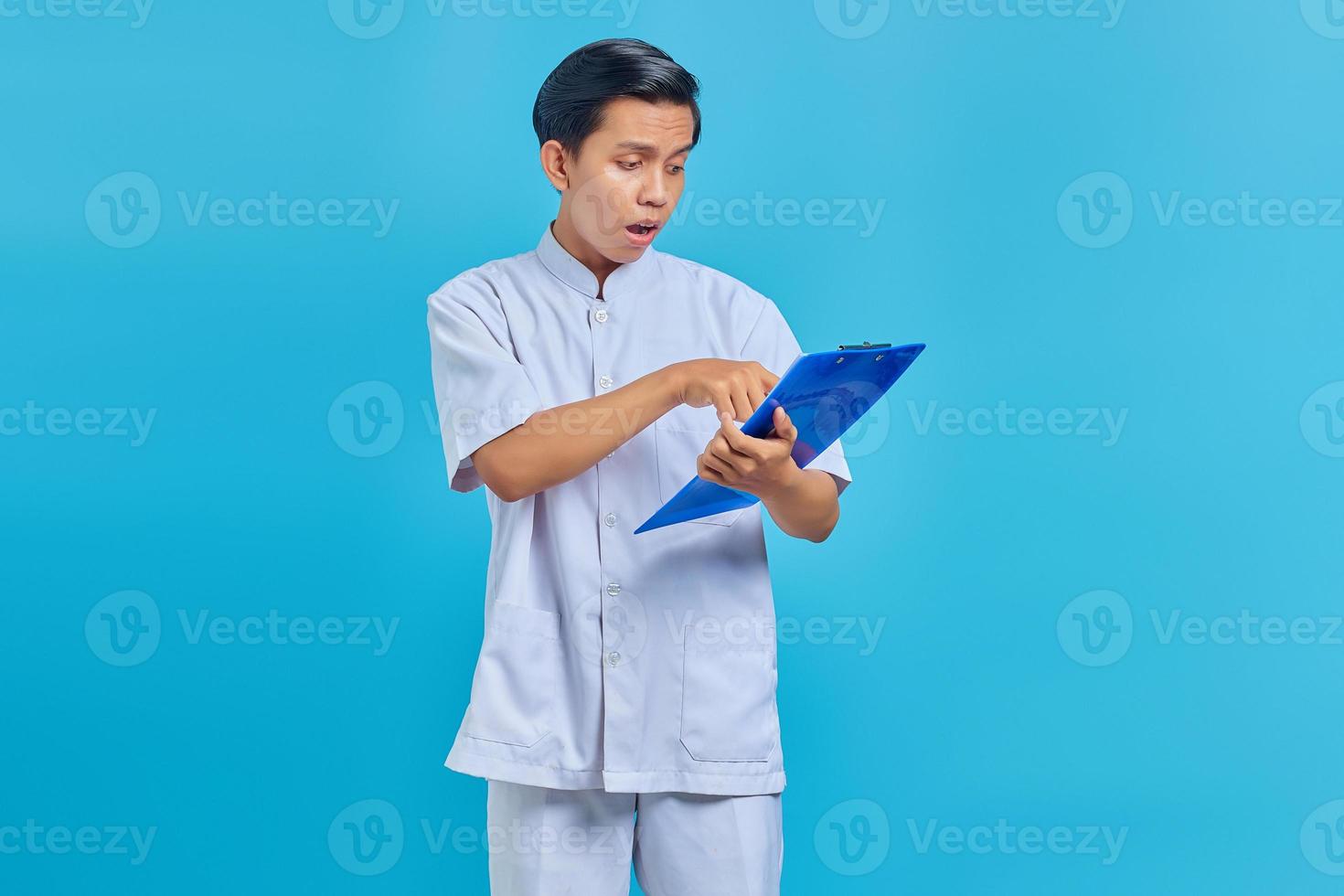 surpris jeune infirmier pointant sur des notes sur le presse-papiers sur fond bleu photo