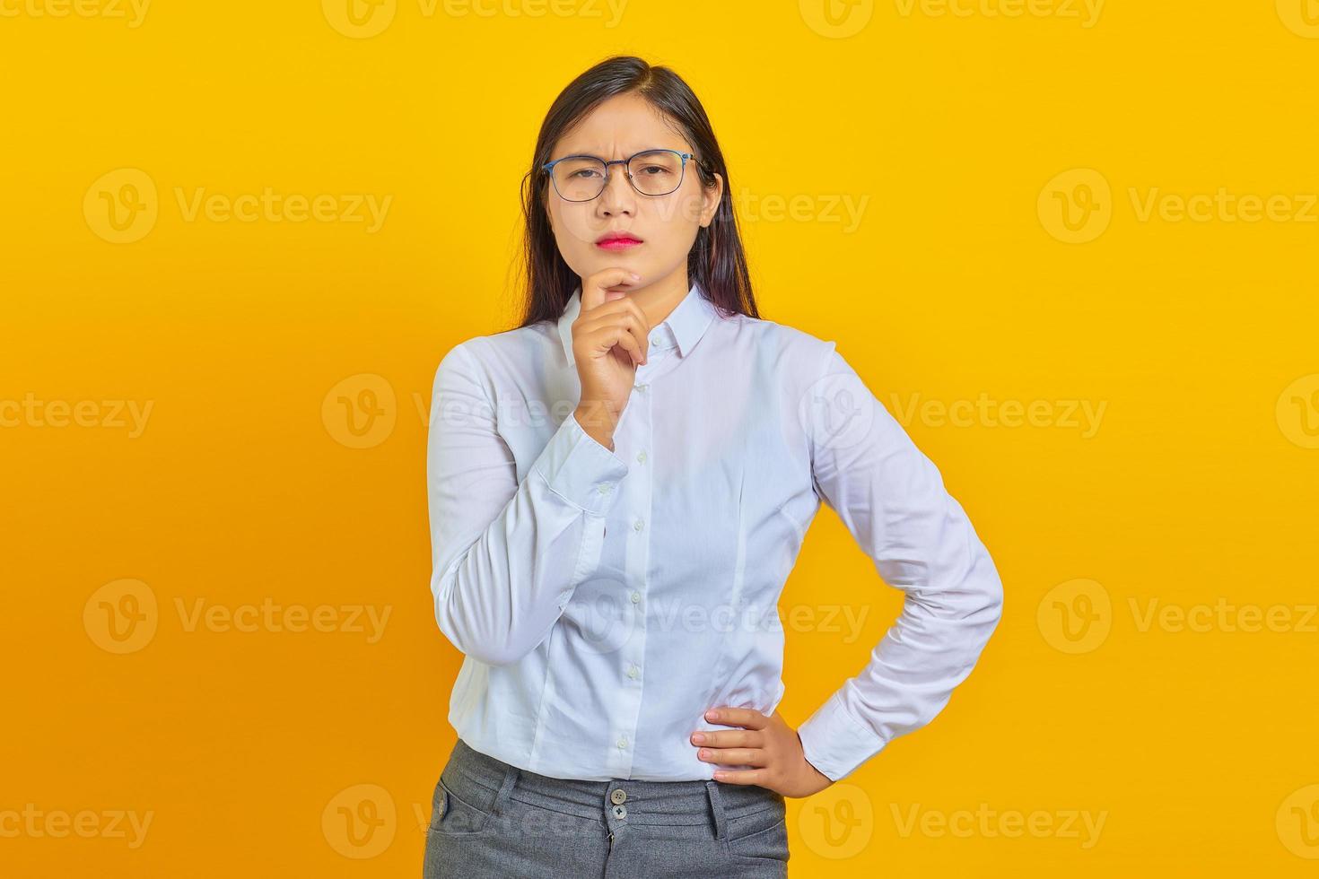 Une jeune femme d'affaires pensive frotte le menton et réfléchit à la question sur fond jaune photo