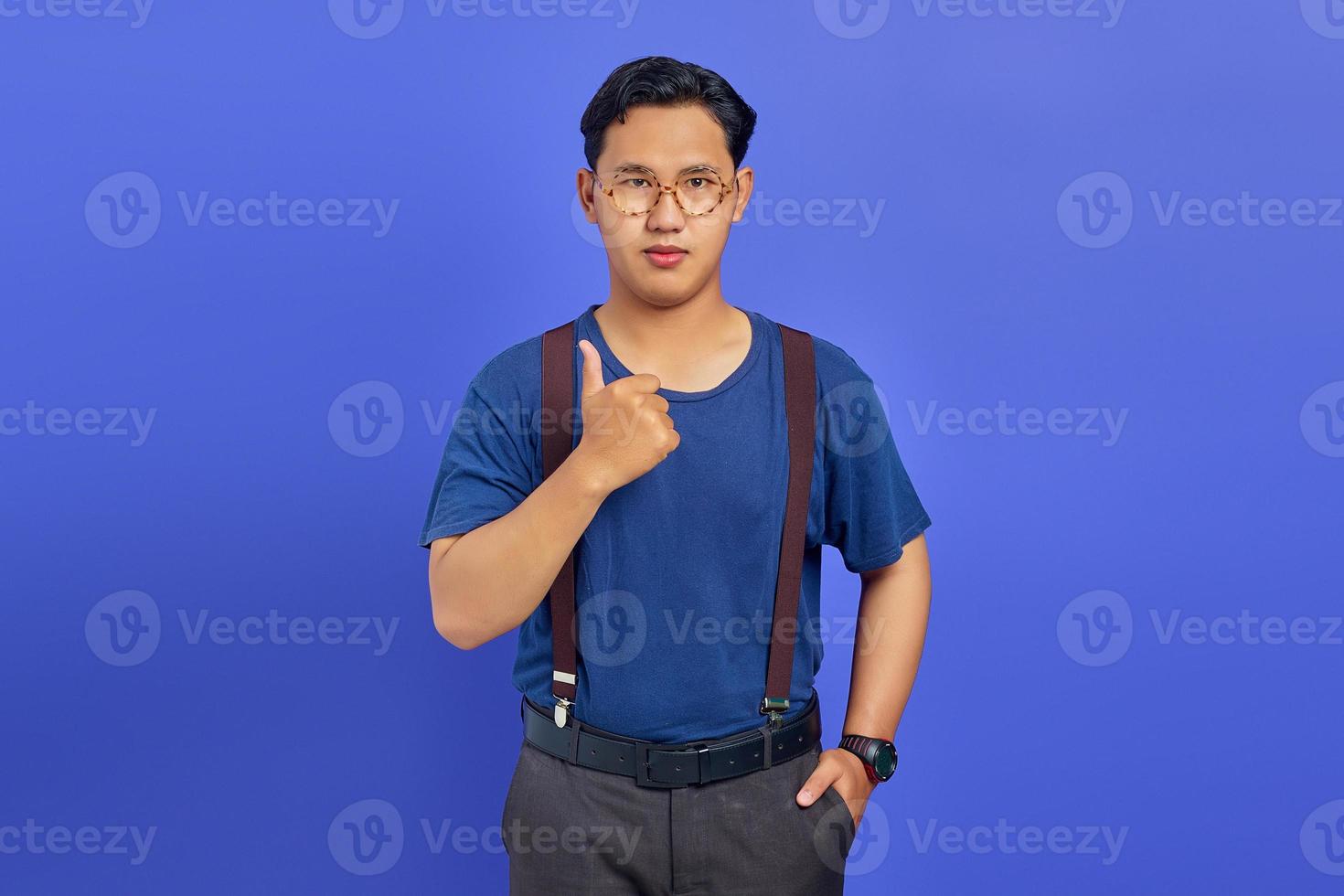 Portrait d'un homme asiatique souriant montrant des pouces vers le haut ou un signe d'approbation isolé sur fond violet photo