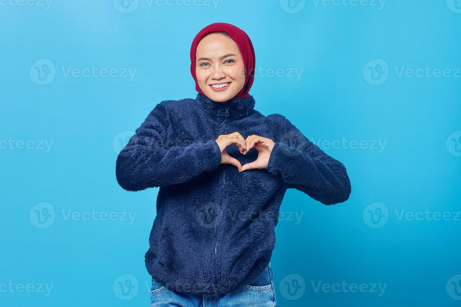 Portrait d'une jeune femme asiatique joyeuse faisant un signe de coeur avec les mains du doigt sur fond bleu photo