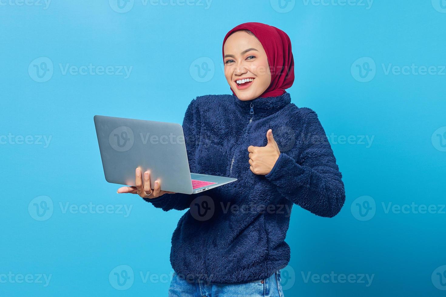 belle femme asiatique utilisant un ordinateur portable souriant et montrant un signe de pouce levé sur fond bleu photo