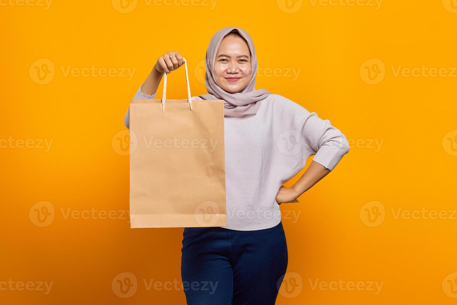 Portrait d'une femme asiatique joyeuse tenant un sac à provisions sur fond jaune photo