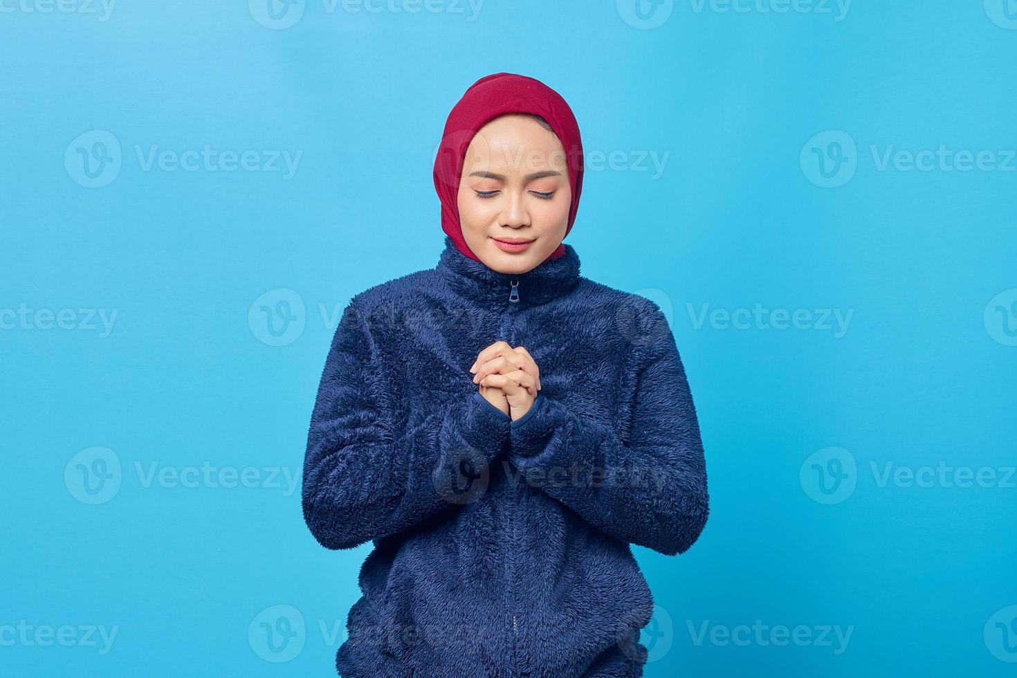 jolie jeune femme asiatique prier et fermer les yeux sur fond bleu photo