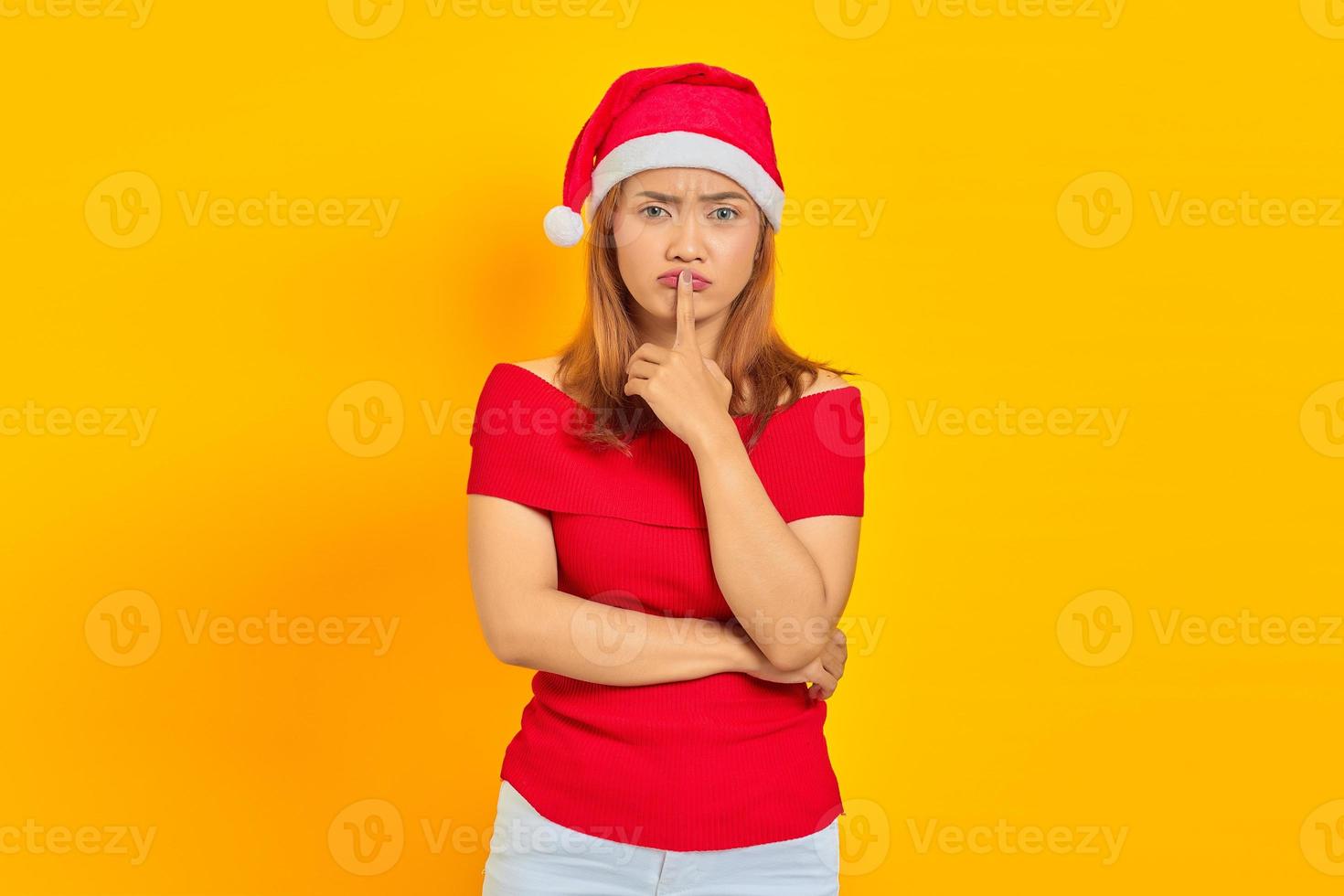 jolie jeune femme asiatique portant un chapeau de noël et faisant un geste de silence sur fond jaune photo