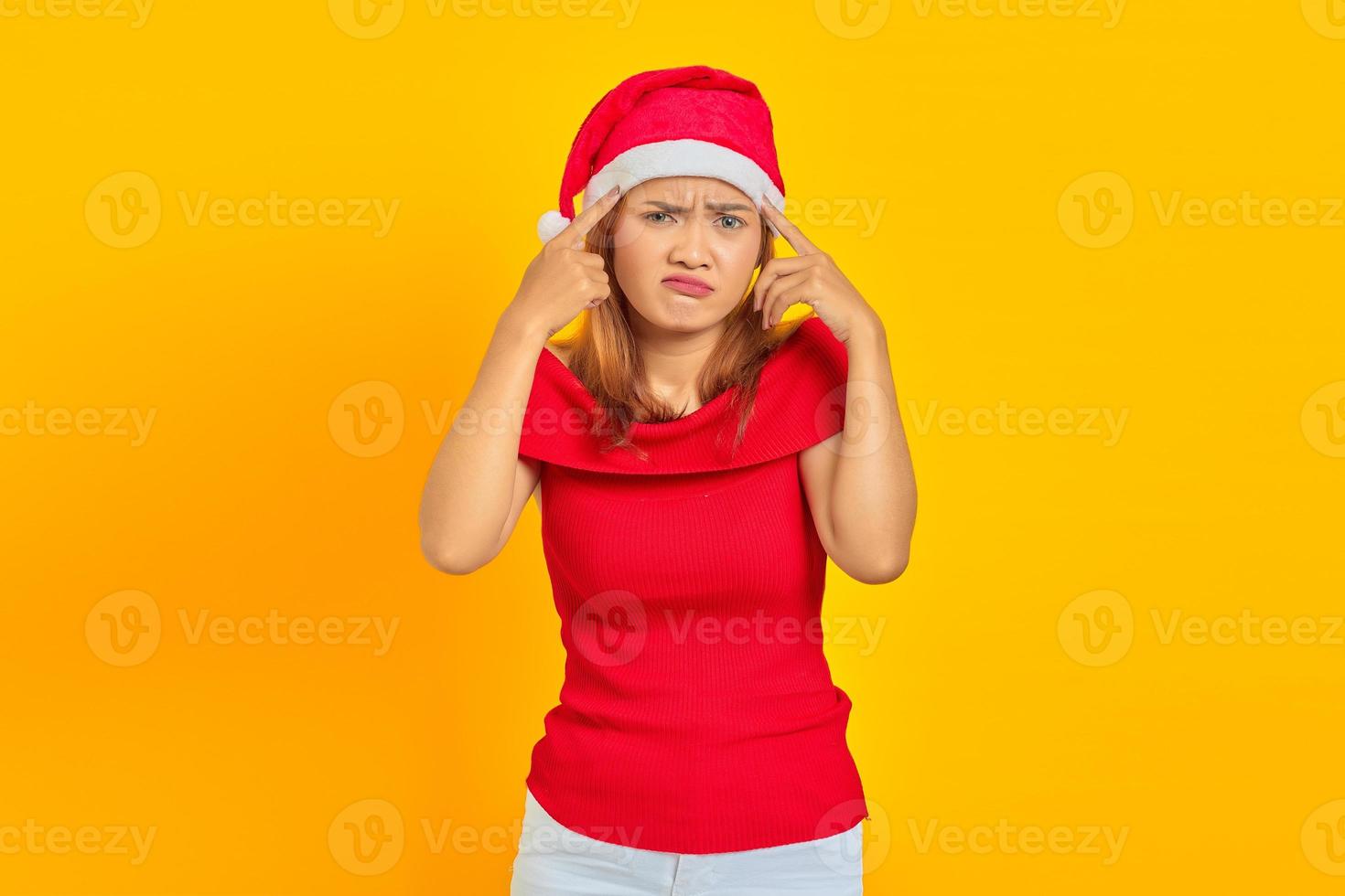 portrait d'une jeune femme pensive portant un chapeau de noël ayant des doutes et pensant sur fond jaune photo