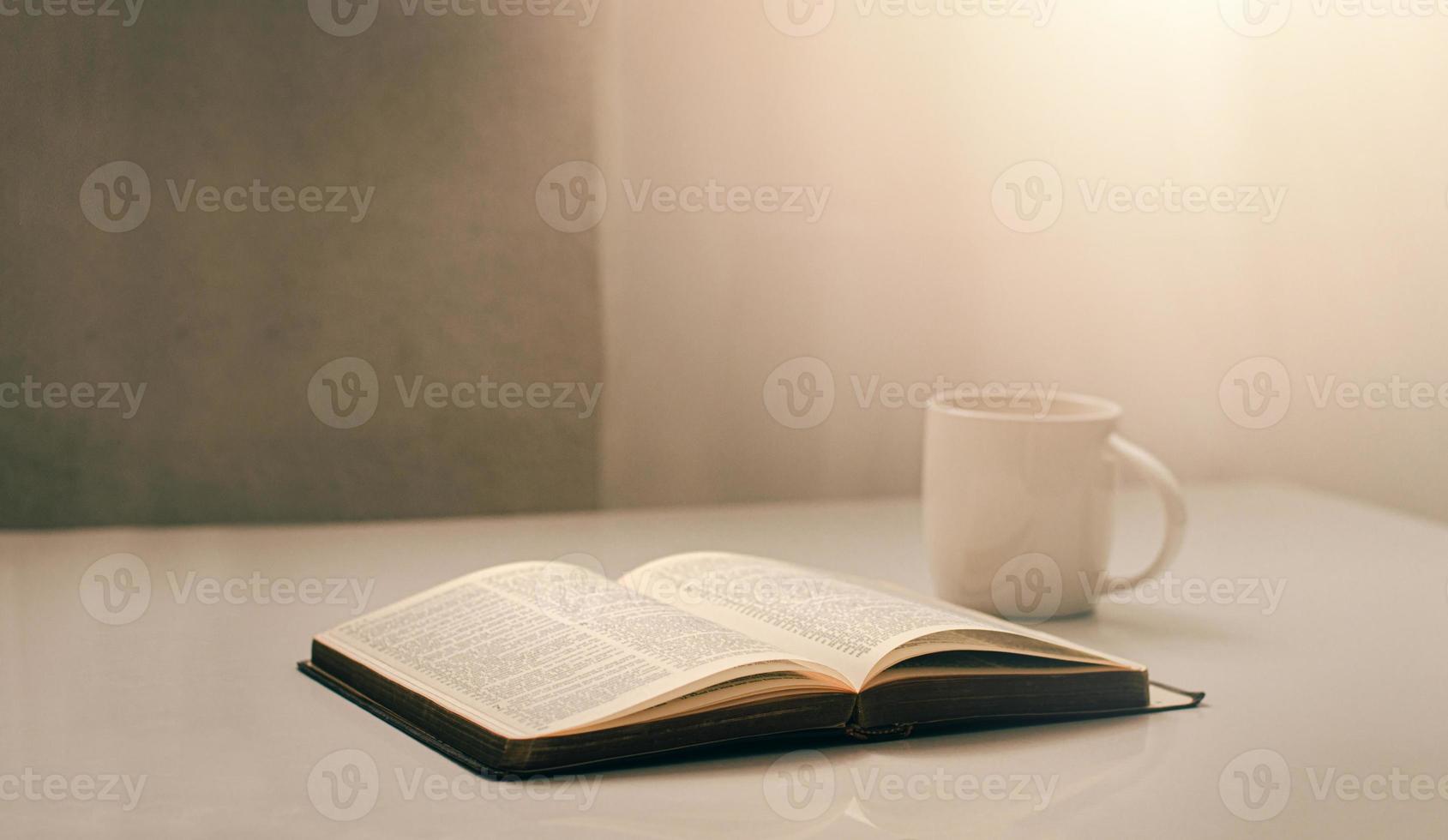 ouvrez une bible près de la fenêtre avec une tasse de café pour la lumière du matin. et posez-le sur une table en bois avec une lumière de fenêtre photo