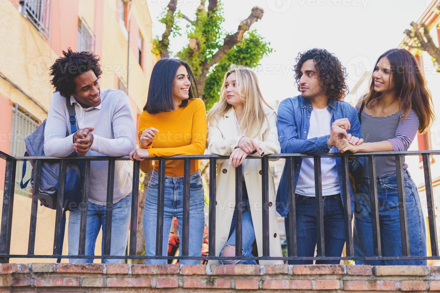 groupe multiethnique d'amis réunis dans la rue appuyés sur une balustrade. photo