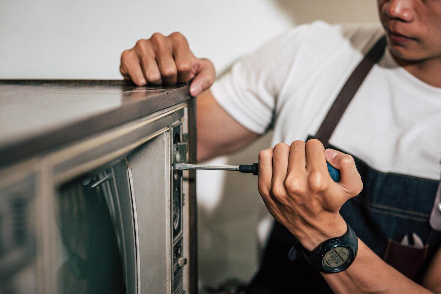 le mécanicien utilise un tournevis pour serrer les vis sur le téléviseur. photo