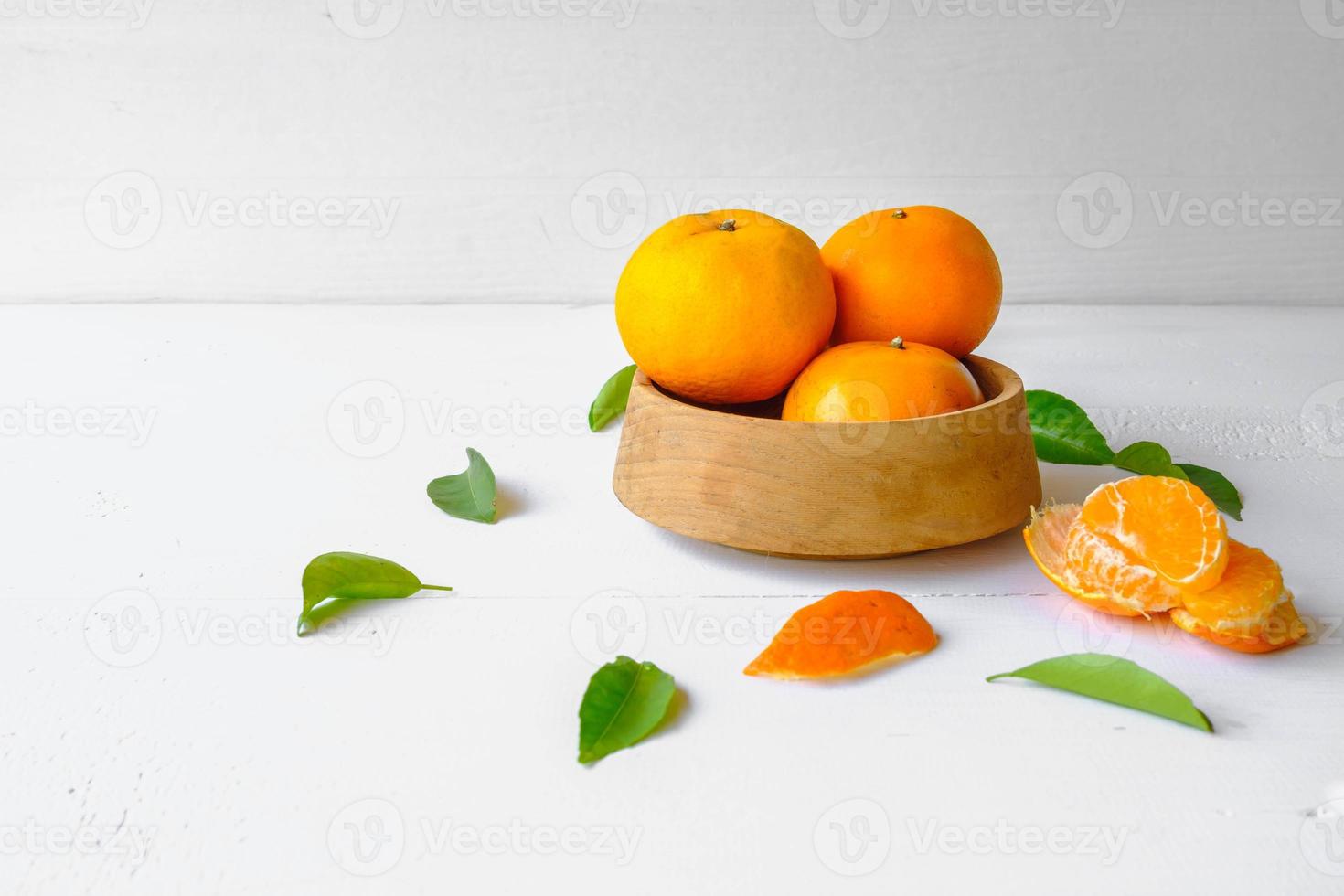 Fruits oranges frais dans un bol en bois sur fond blanc photo