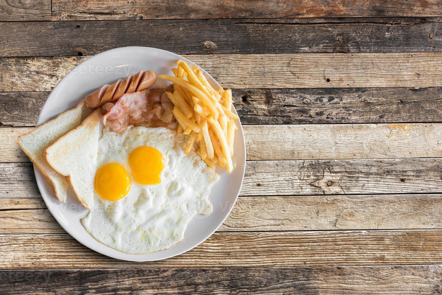 vue de dessus du petit-déjeuner américain avec des œufs brouillés, du bacon, du pain grillé, des frites et des saucisses sur fond de table en bois. photo