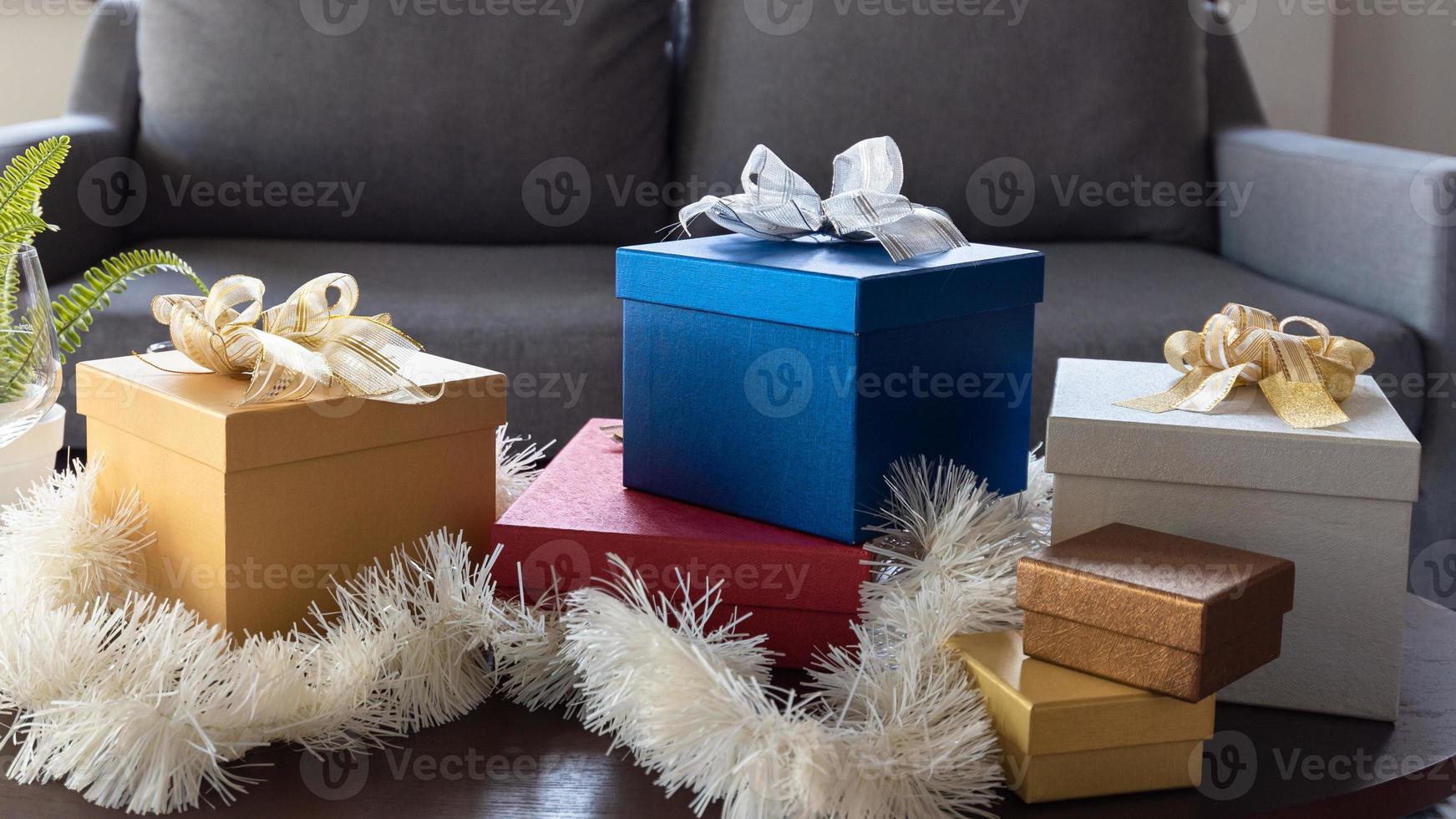 Belles boîtes-cadeaux de Noël enveloppées dans du papier coloré avec un nœud en ruban sur une table dans le salon à la maison photo