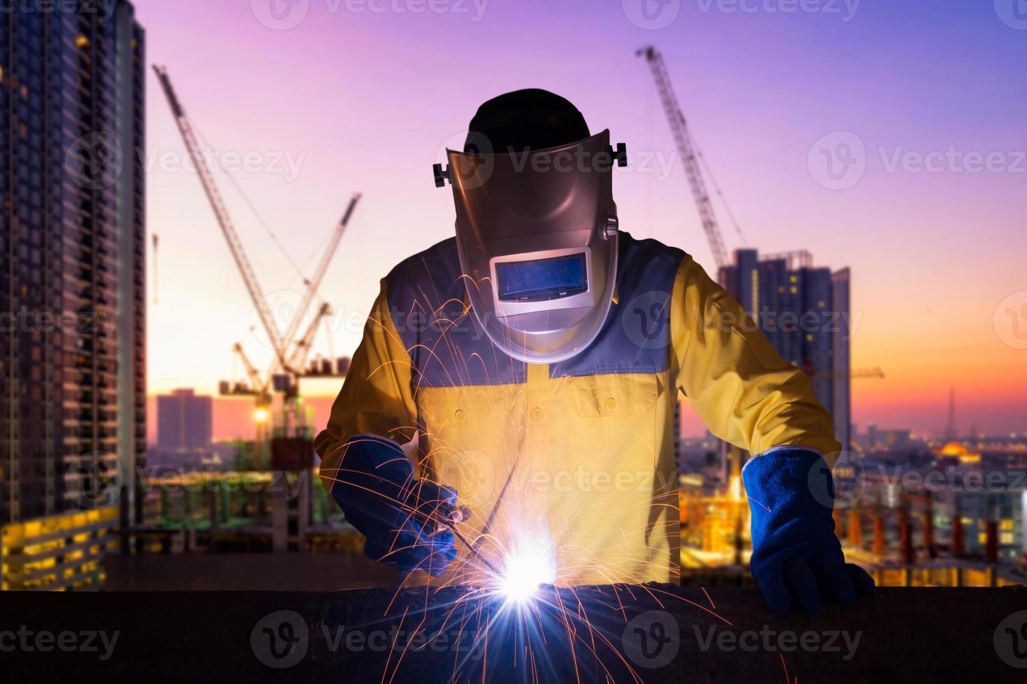Ouvrier industriel soudant une structure en acier pour un projet de construction d'infrastructures avec un chantier de construction en arrière-plan. photo