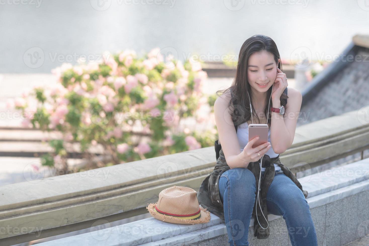 belle femme touristique solo asiatique se relaxant et appréciant d'écouter de la musique sur un smartphone dans le centre-ville de la ville urbaine. voyage de vacances en été. photo