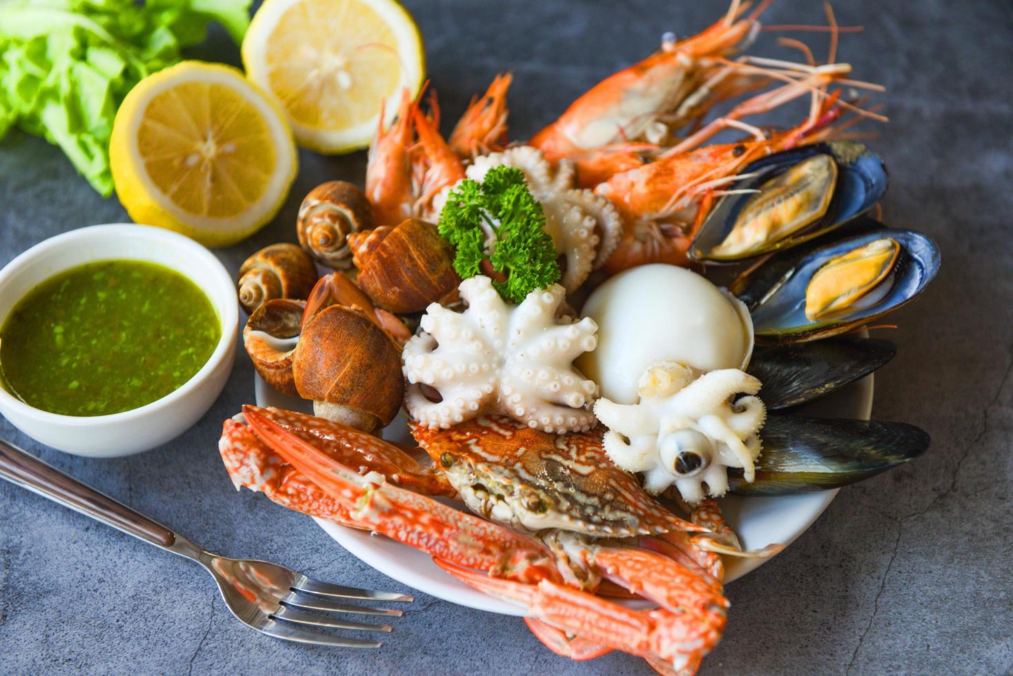 concept de buffet de fruits de mer servi à la vapeur - crevettes fraîches crevettes calamars moules tachetées de babylone crustacés crabe et sauce aux fruits de mer citron sur assiette fond noir en pierre photo