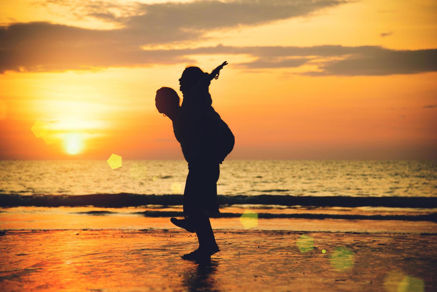 amants asiatiques heureux sur la plage avec un beau coucher de soleil en arrière-plan homme soulevant la femme. photo