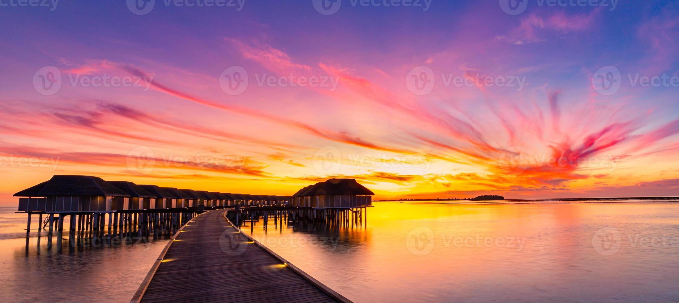 coucher de soleil sur l'île des maldives, complexe de villas sur l'eau de luxe et jetée en bois. beau ciel et nuages et fond de plage pour les vacances d'été et le concept de voyage photo