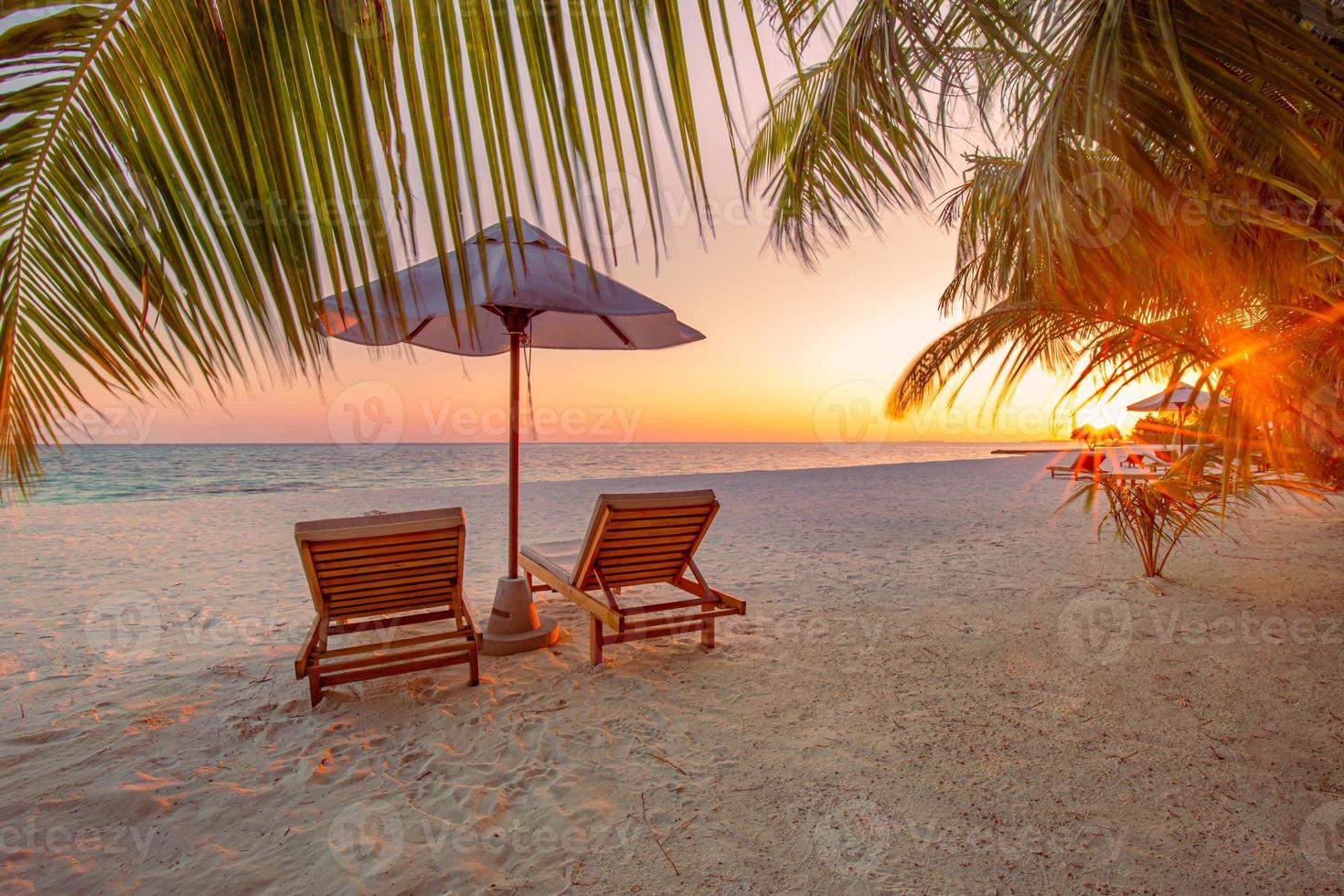 beau paysage tropical de coucher de soleil, deux chaises longues, chaises longues, parasol sous palmier. sable blanc, vue mer avec horizon, ciel crépusculaire coloré, calme et détente. hôtel balnéaire inspirant photo