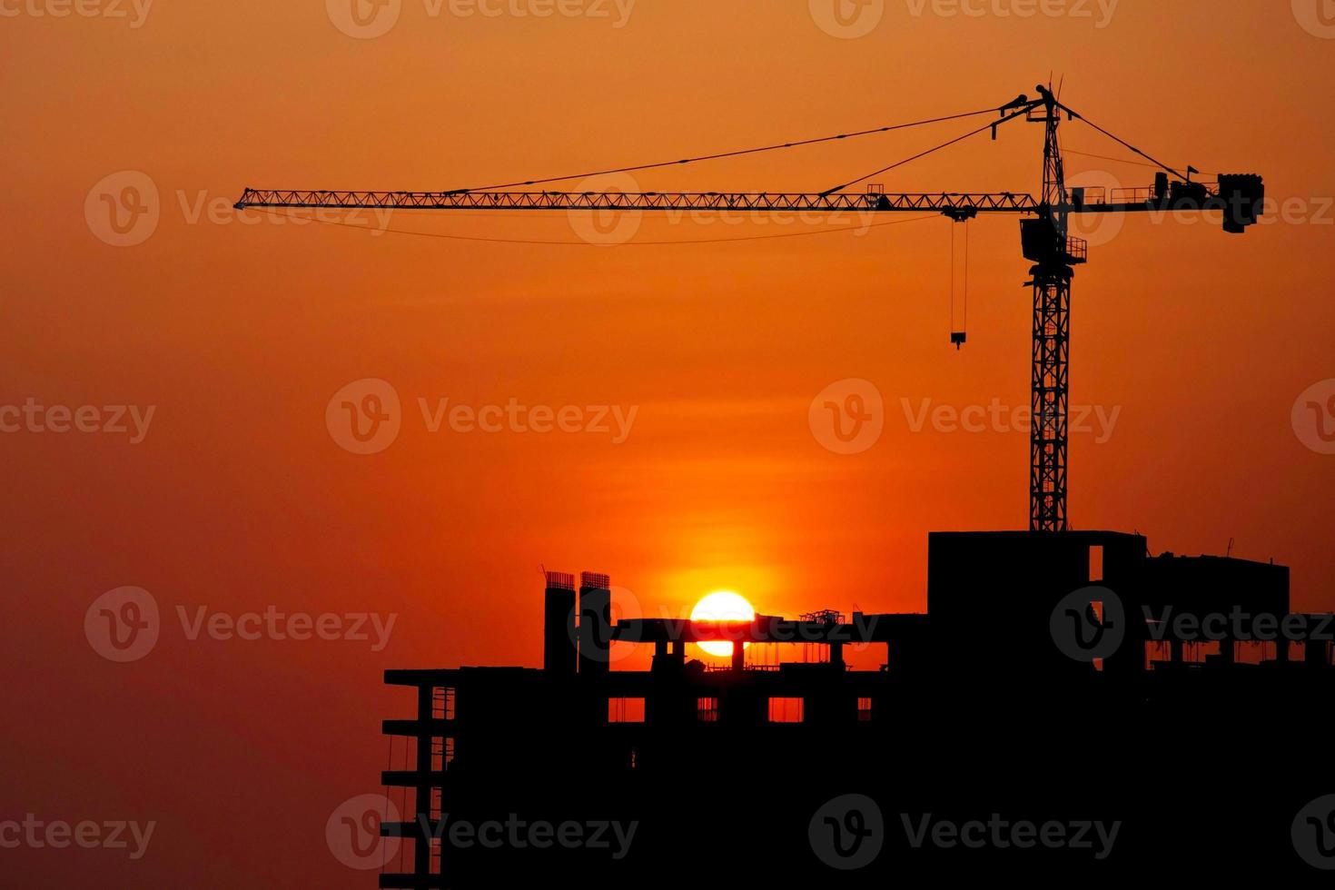 grue de construction silhouettée et bâtiment au chantier de construction au coucher du soleil pour le concept de travail industriel de construction photo