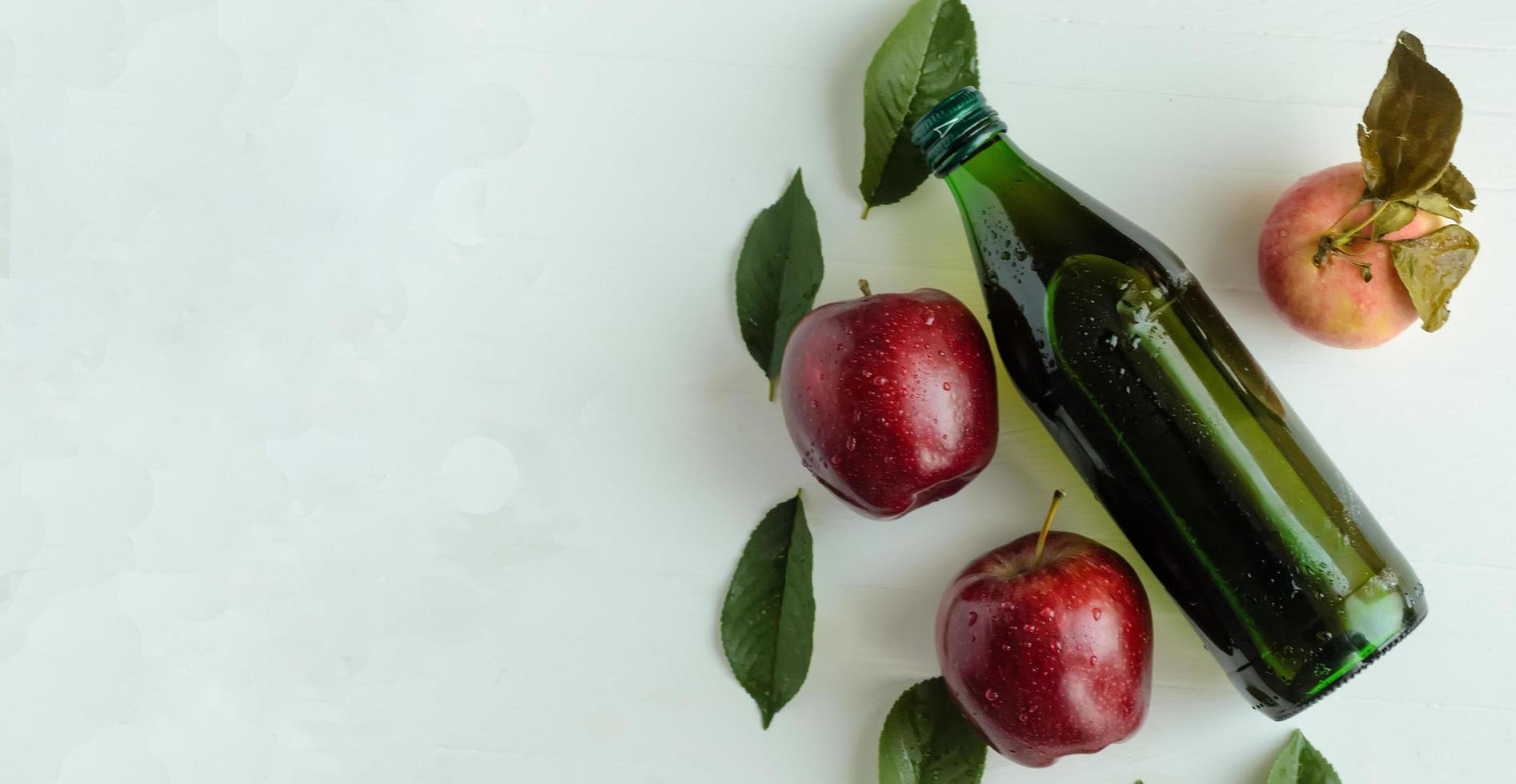 vue de dessus, une bouteille de vinaigre de cidre de pomme avec trois pommes fraîches et feuilles vertes photo