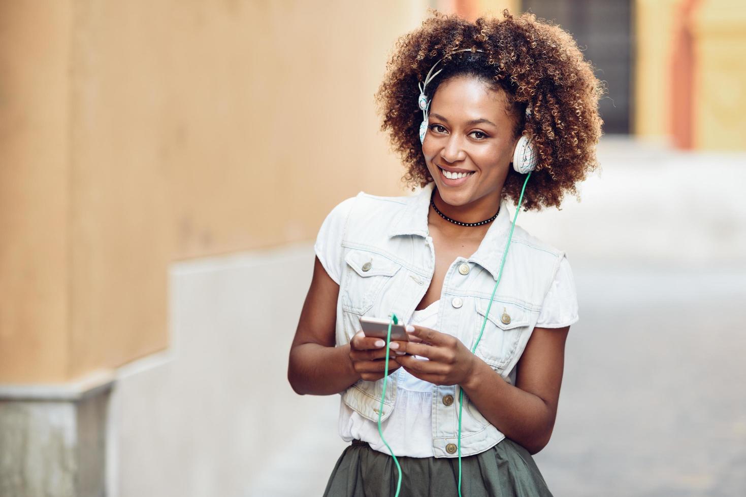 fille noire, coiffure afro, dans la rue urbaine avec casque et smartphone photo