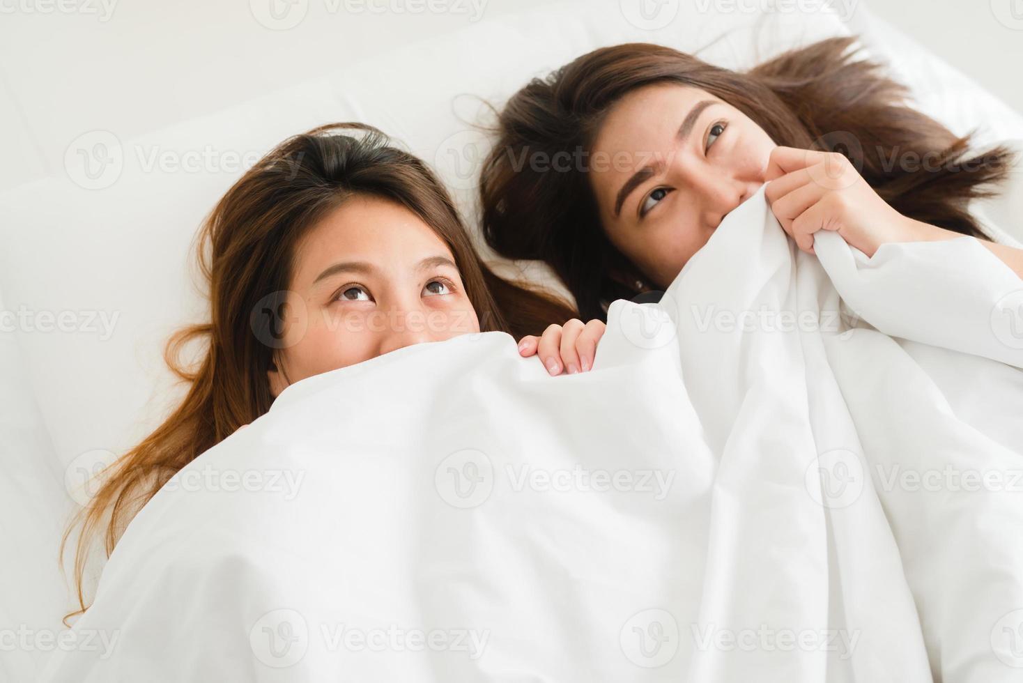 vue de dessus de belles jeunes femmes asiatiques couple heureux lesbien montrant la surprise et regardant la caméra en position couchée dans son lit sous une couverture. femmes drôles après le réveil. concept de couple de lesbiennes ensemble à l'intérieur photo