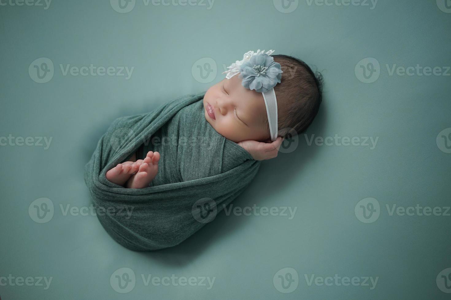 petit nouveau-né enveloppé d'une écharpe bleue avec un bandage sur la tête se trouve sur une couverture douce photo