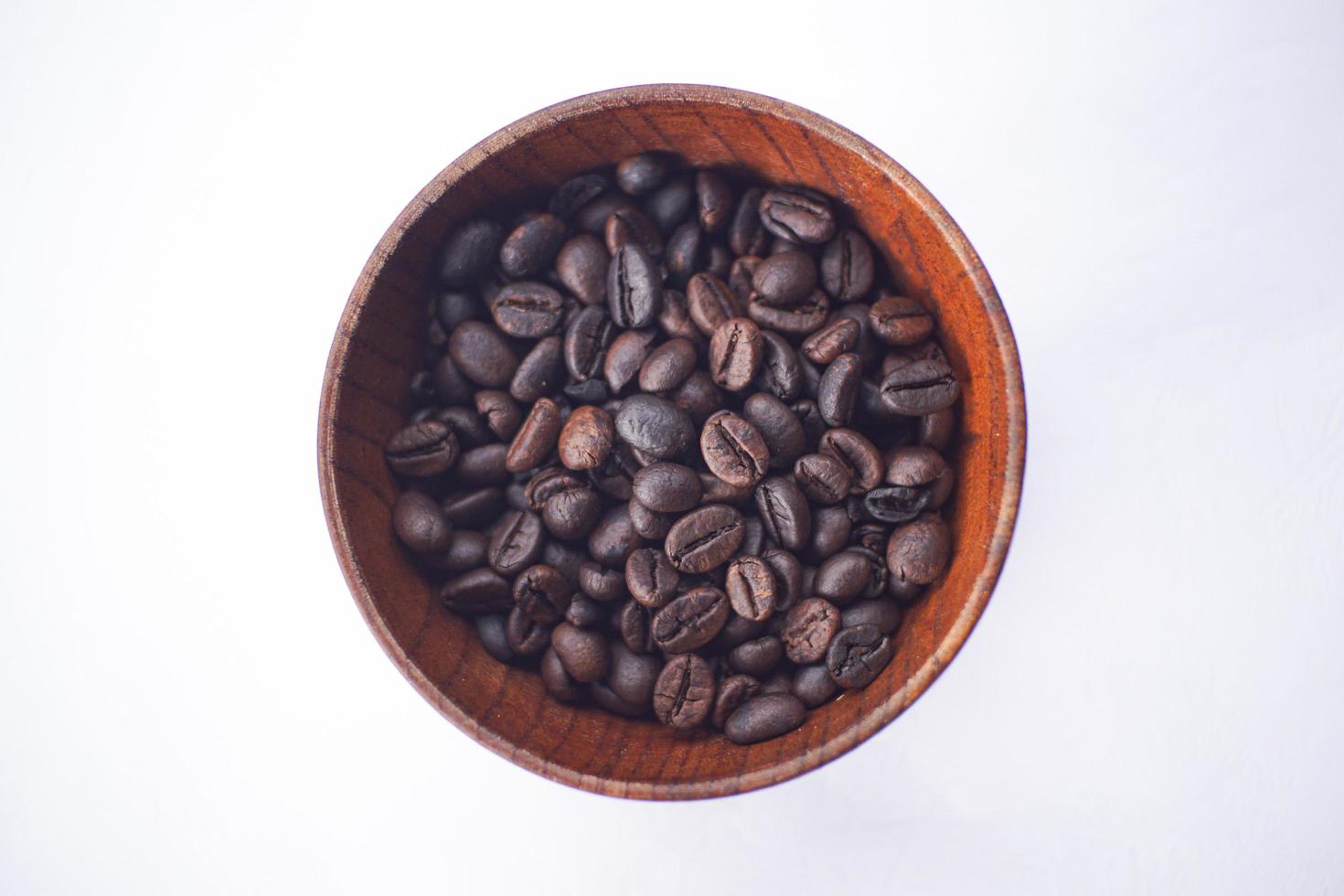 grains de café dans un bol en bois sur une table blanche photo