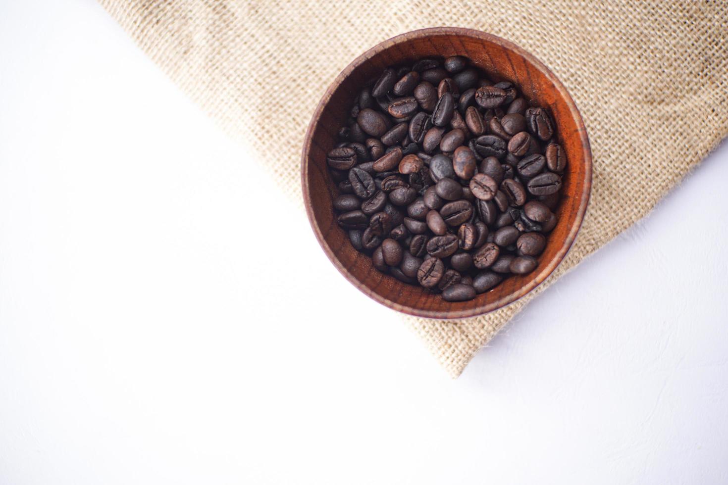 grains de café dans un bol en bois sur une table blanche photo