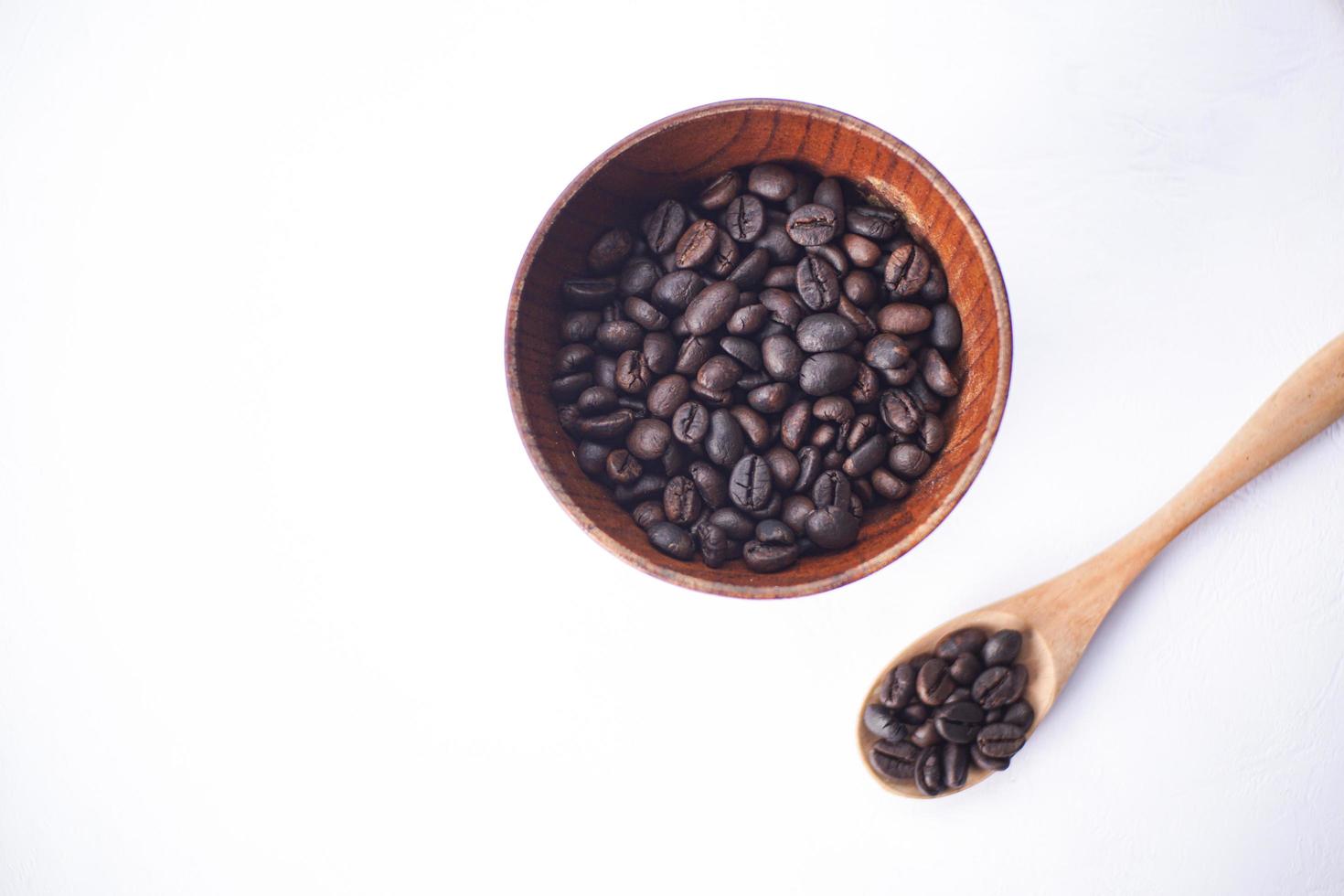 grains de café dans un bol en bois sur une table blanche photo