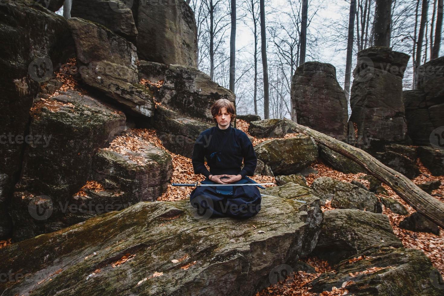 l'homme en kimono noir avec une épée médite et se concentre sur les rochers et le fond de la forêt photo