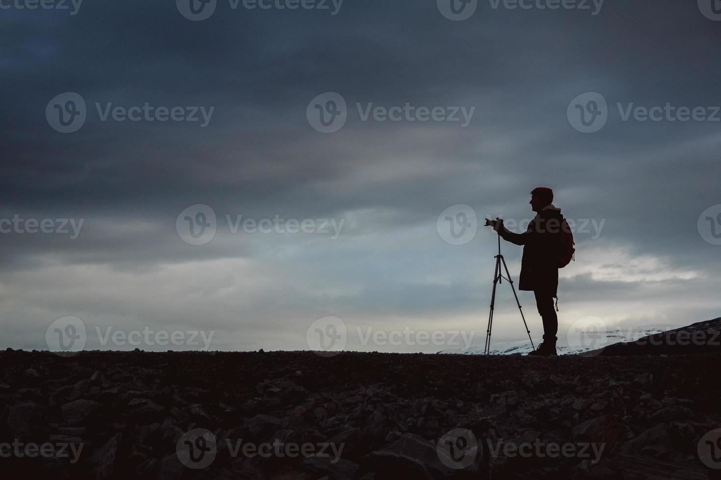 silhouette d'homme voyageur avec appareil photo sur trépied sur fond de ciel dramatique