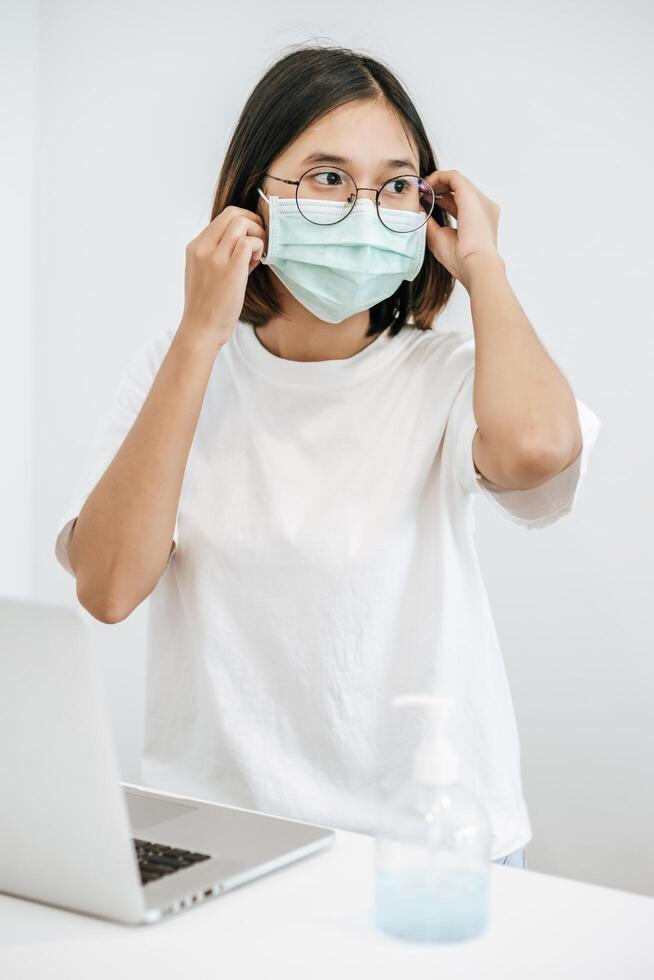 les femmes portant des masques sanitaires ont un ordinateur portable sur la table et du gel pour se laver les mains. photo