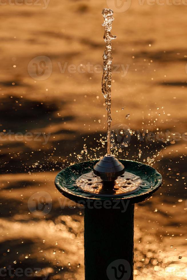 fontaine à eau qui coule sur la plage près du lac au coucher du soleil photo