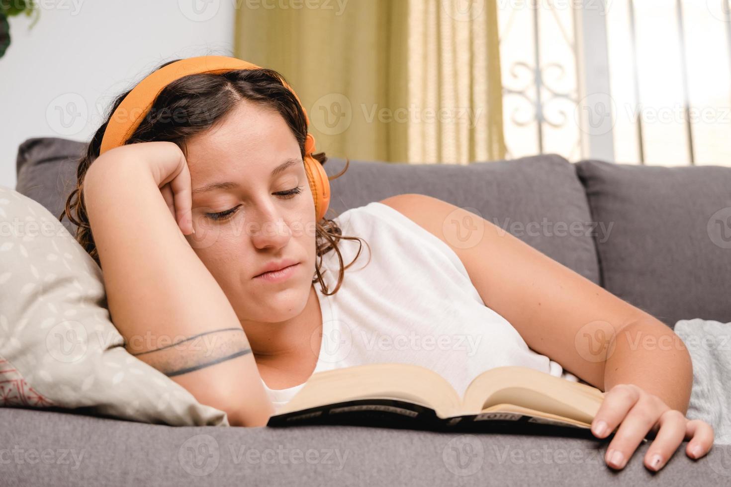 femme avec des écouteurs lisant un livre dans le salon assis sur le canapé photo