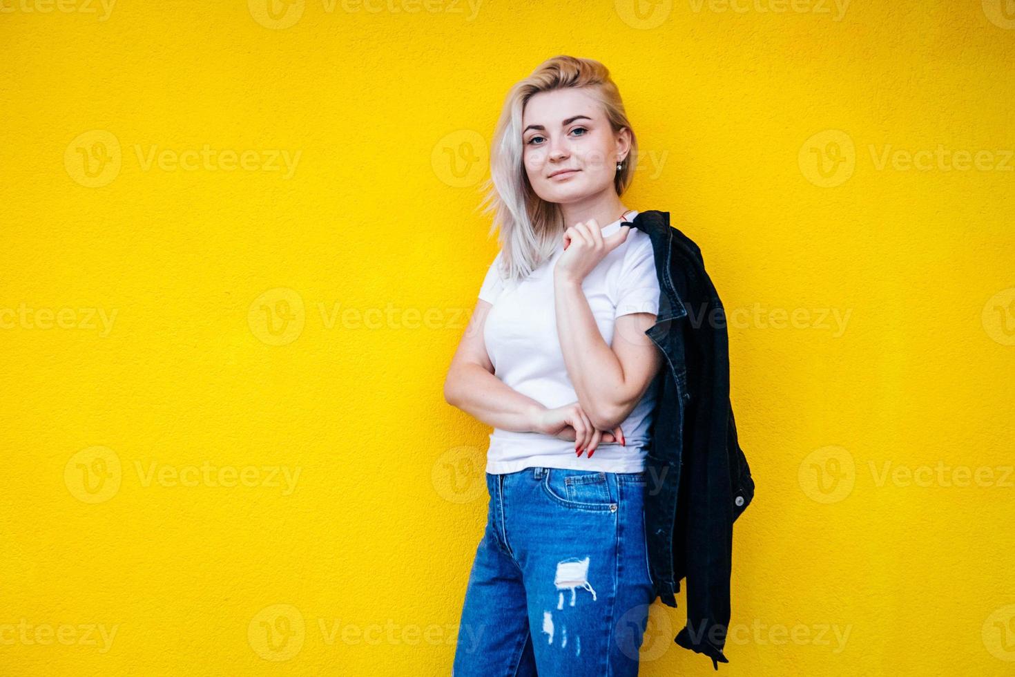 femme en veste noire souriante posant sur fond de mur jaune photo