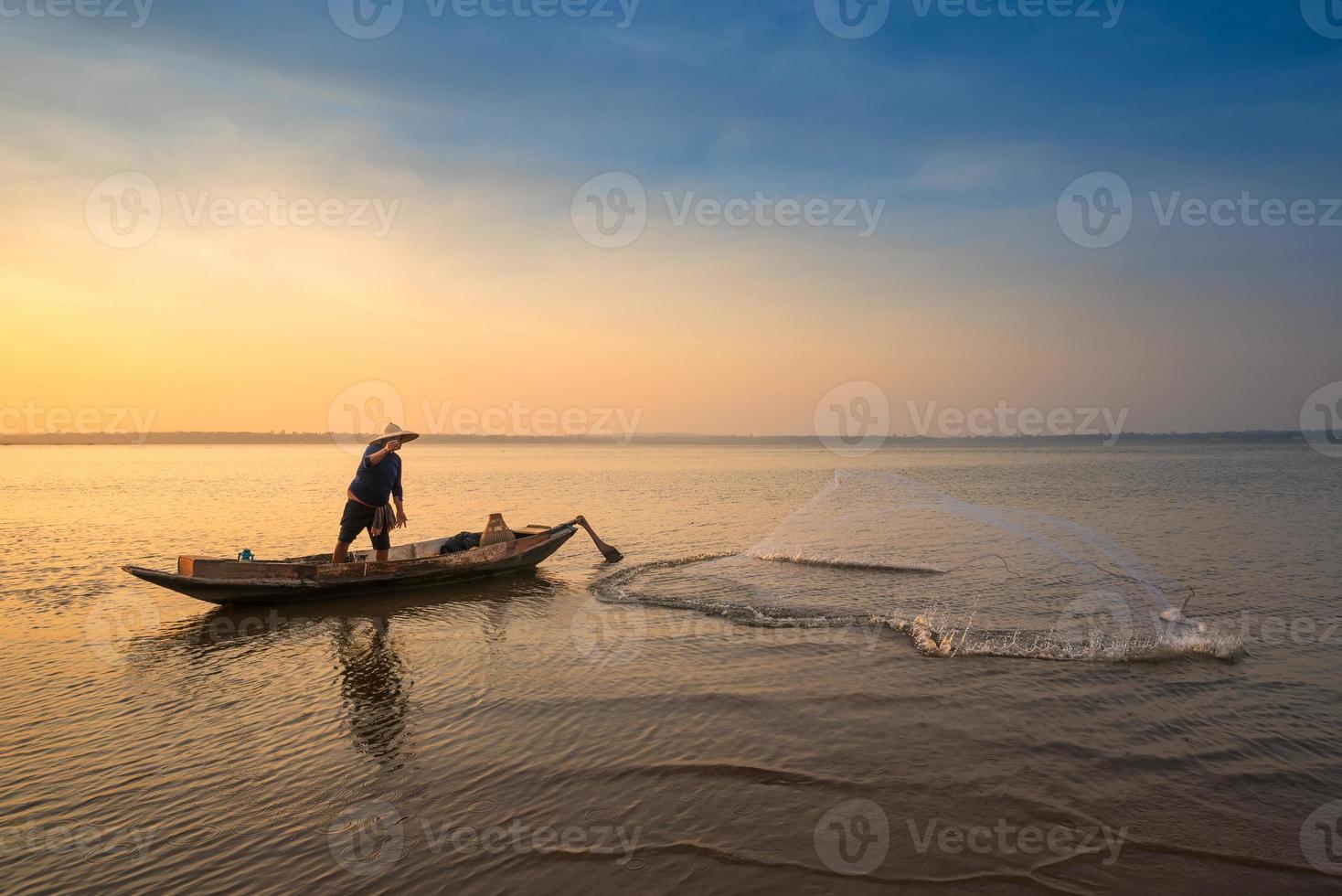 pêcheur asiatique sur un bateau en bois jetant un filet pour attraper des poissons d'eau douce dans la rivière naturelle tôt le matin avant le lever du soleil photo