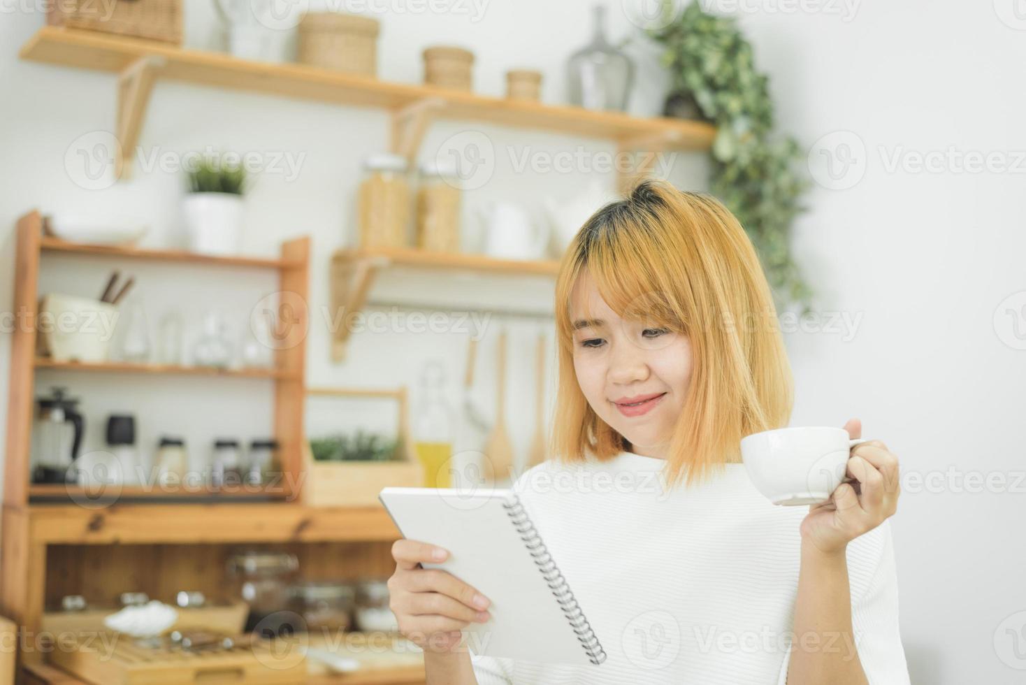 une femme asiatique écrit des listes de courses dans le bloc-notes au stylo sur son comptoir de cuisine à la maison et lit et essaie de se souvenir de tous les ingrédients pour faire ses courses à l'épicerie. les femmes de style de vie se détendent à la maison concept. photo