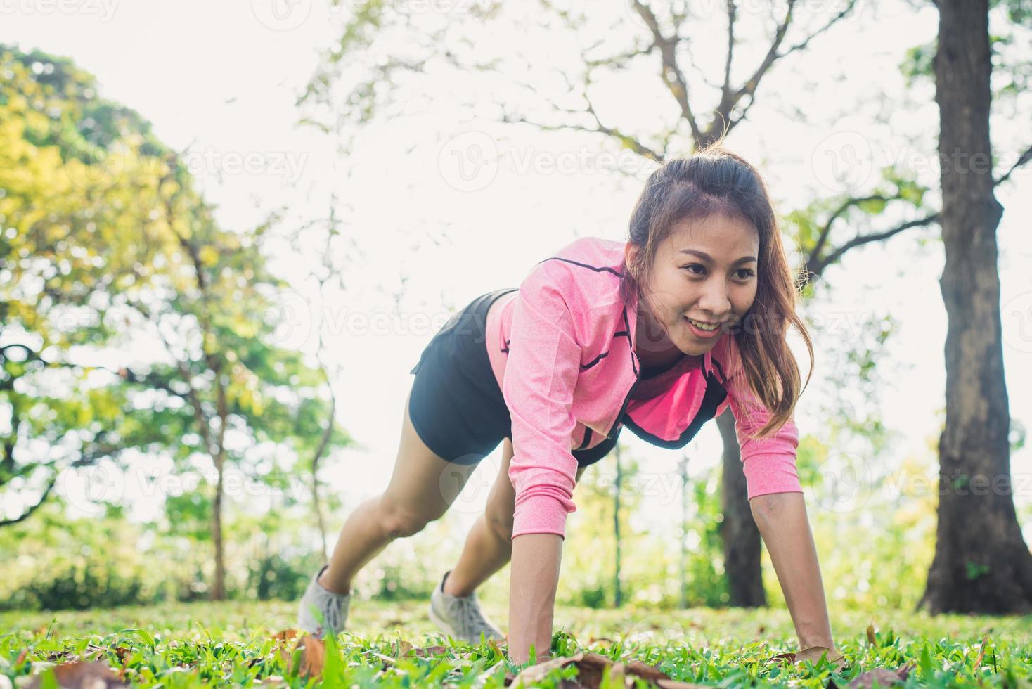 jeune femme asiatique réchauffe son corps en poussant pour développer sa force avant l'exercice de jogging matinal et le yoga sur l'herbe sous le soleil chaud et léger du matin. exercer le concept de plein air. photo