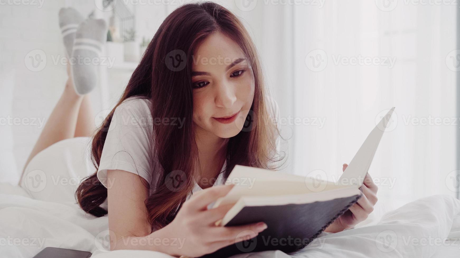 Portrait de la belle femme asiatique attrayante, lisant un livre en position couchée sur le lit lorsque vous vous détendez dans sa chambre à la maison. femmes de mode de vie utilisant le temps de détente au concept de la maison. photo