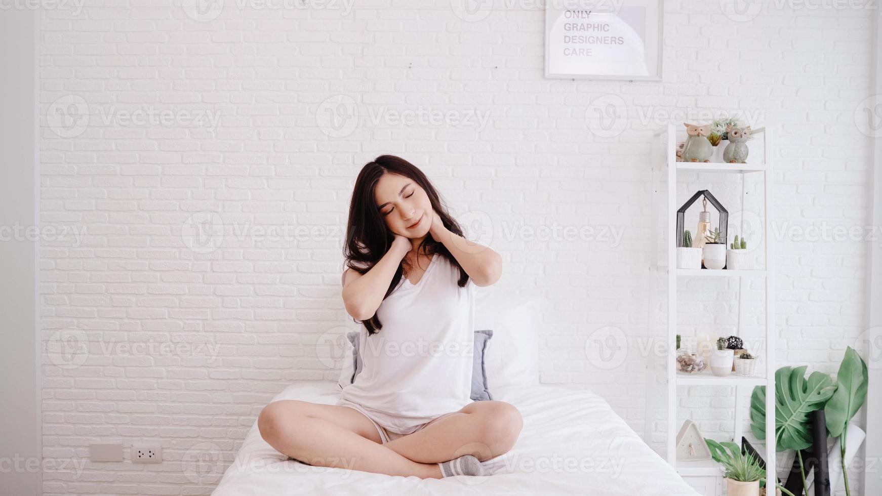 belle femme asiatique étirant son corps après s'être réveillée dans sa chambre à la maison. une femme heureuse profite d'une matinée ensoleillée. femme de style de vie à la maison concept. photo