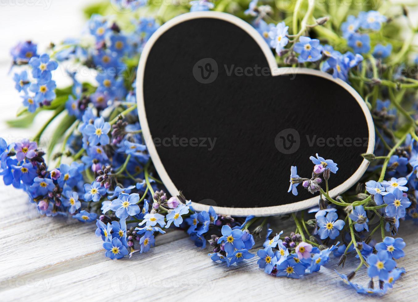 fleurs myosotis et tableau en forme de coeur noir sur fond de bois blanc photo