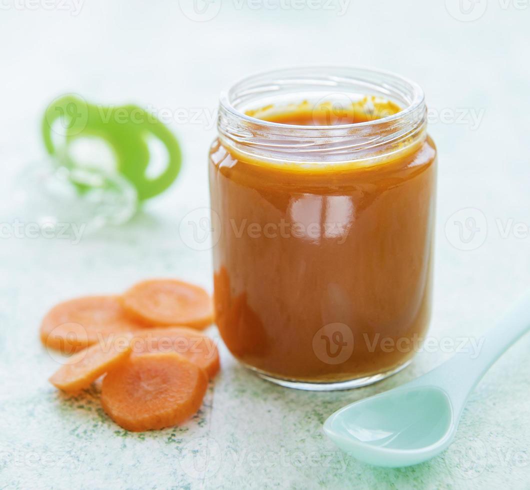 Bébé carotte en purée avec cuillère dans un bocal en verre photo