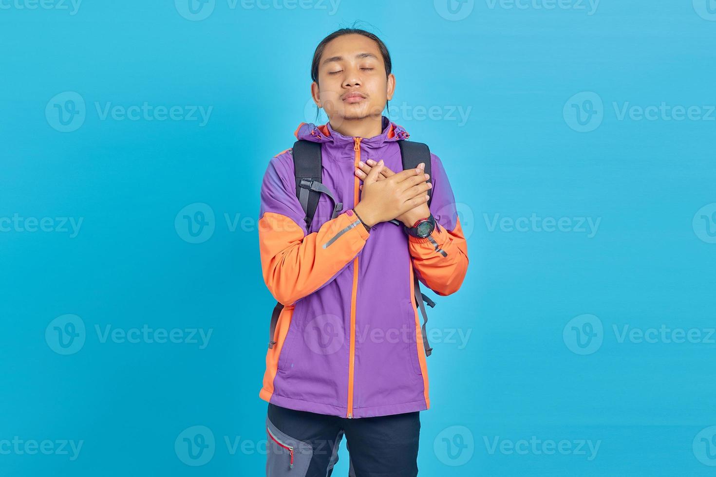 portrait d'un bel homme asiatique avec les deux paumes sur la poitrine et les yeux fermés sur fond bleu photo