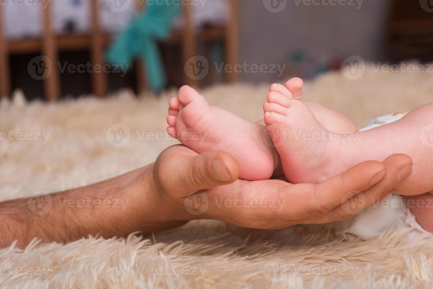 papa tient dans ses mains un petit baby foot. petites jambes d'un nouveau-né dans les grandes mains de papa. massage des pieds de bébé photo